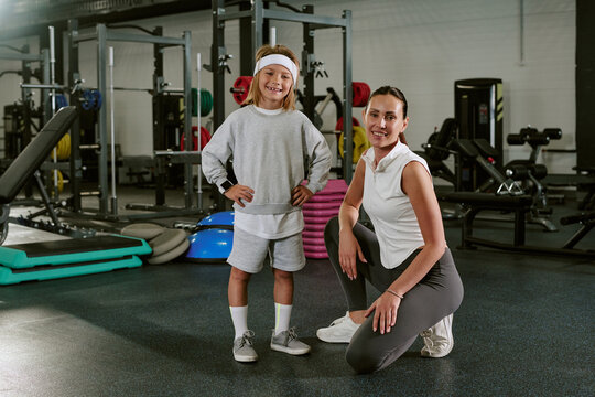 Portrait of smiling Caucasian female trainer and child posing in gym. Image is suitable for promoting youth fitness programs, family wellness memberships, and healthy lifestyle habits