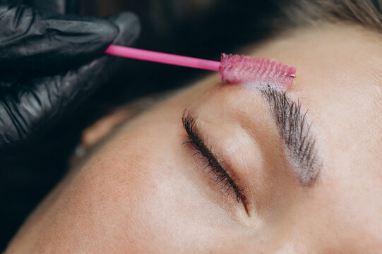Close-up of a beauty specialist applying lamination solution to a clients eyebrow with a spoolie brush during a professional brow treatment.