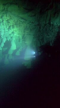 A green-white beam illuminates an uneven submerged wall and surrounding darkness in Cenote Zapote, Quintana Roo, Mexico.