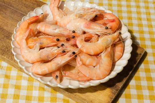 Boiled unshelled tiger shrimps on plate on yellow white tablecloth. Seafood.