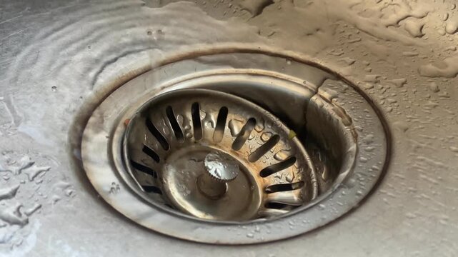 Overhead view of tap water flowing into a kitchen sink drain