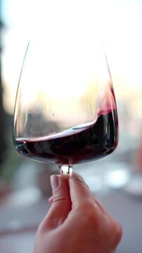 Person holding glass of red wine and swirling liquid to aerate it for tasting.