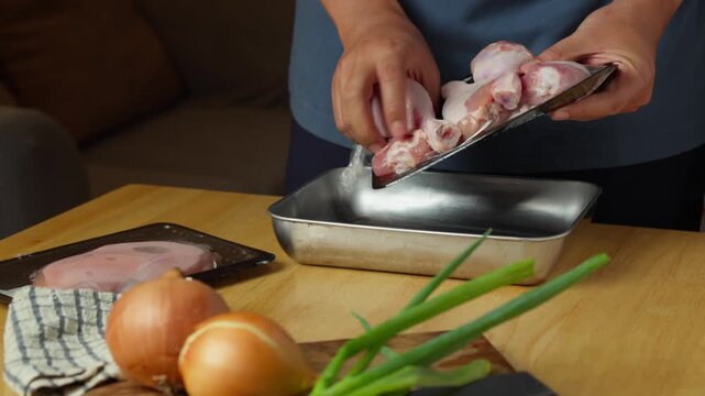 Person transferring fresh raw chicken drumsticks from a package into a stainless steel tray before seasoning and marinating