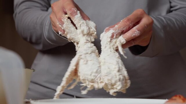 hands gently shaking and draining excess flour from breaded chicken drumsticks during the fried chicken preparation process