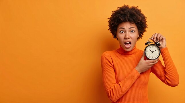 An excited young lady with curly hair holds a clock, expressing shock as time is running out. yellow background with copy space, perfect for urgency concepts.