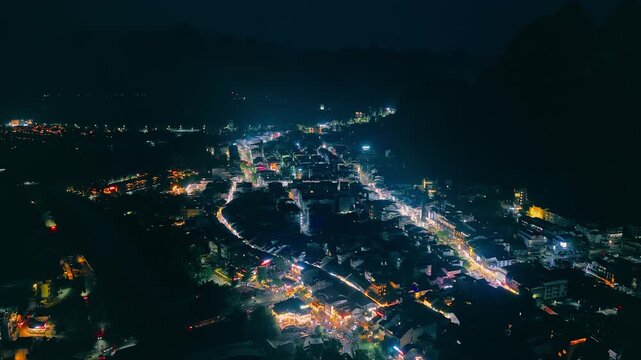Bright city lights trace a town among karst mountains near Guilin, China, viewed from above at night, supporting tourism and travel themes.