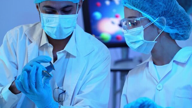 Two scientists in lab coat wearing protective gear examining microchip component carefully while collaborating on technology development project in laboratory
