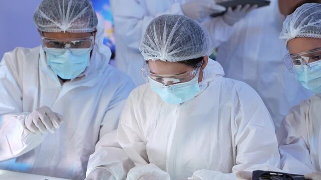 Group of semiconductor engineer wearing cleanroom protective suit mask safety goggle examining microchip component and silicon wafer during development process
