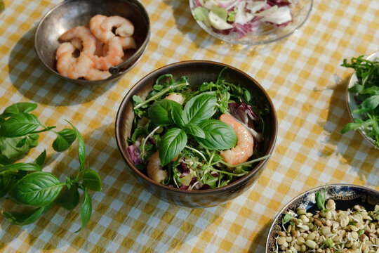Seasonal summer salad with shrimps garnished with basil leaf on yellow white tablecloth. Heathy dinner. Mediterranean kitchen. 