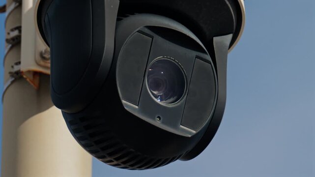 Security surveillance camera rotating on metal pole for monitoring public area and perimeter safety.