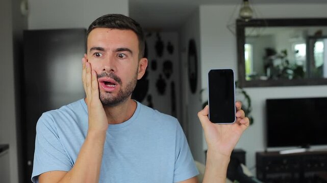 Handsome man showing modern smartphone screen directly on camera with surprise 