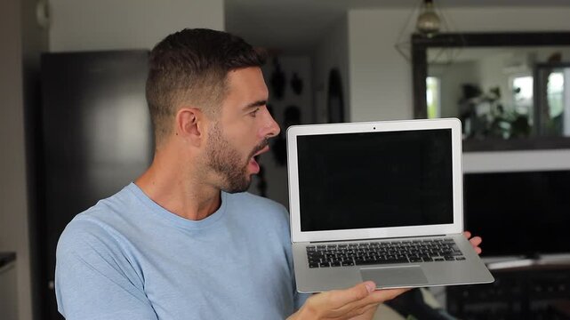 Shocked man opening modern laptop computer and opening his mouth at camera screen while seeing something shocking