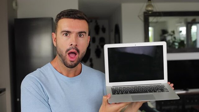 Shocked man opening modern laptop computer and opening his mouth at camera screen while seeing something shocking