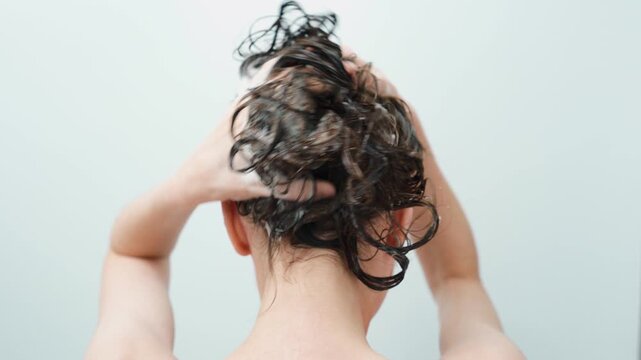 Woman washing her soapy hair with shampoo, rear view in bathroom. Scalp and hair care. Personal hygiene.