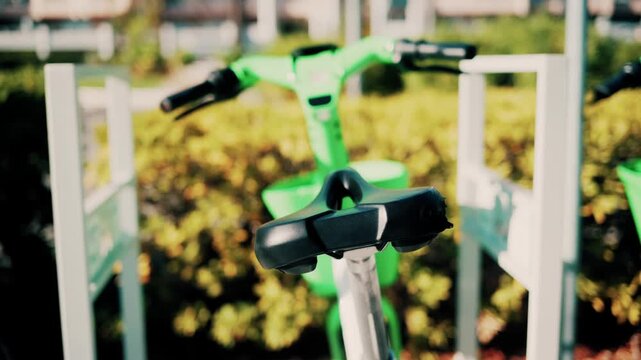 Row of electric rental bicycles parked in urban bike station during sunny day.