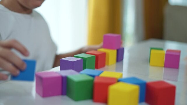 Child playing at table in bright room. Child focused on arranging colorful blocks at house. Indoor activity in cozy house. Child engaging creative play at table. Kid enjoying playtime in well lit room