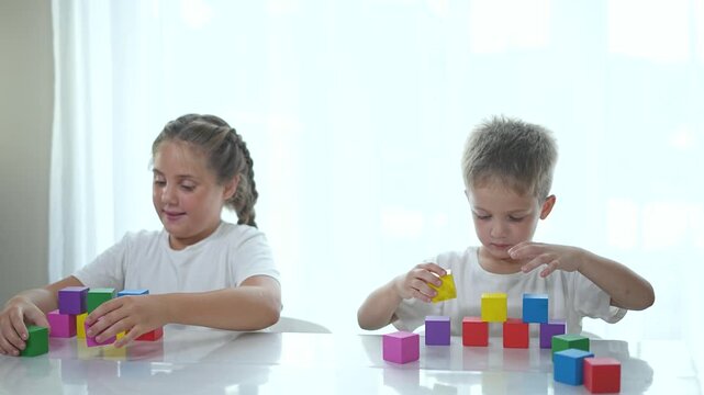 Brother and sister play with blocks at home. Brother and sister build block structures together. Creative playtime with blocks strengthens sibling bond. Children enjoy playful family time with blocks.