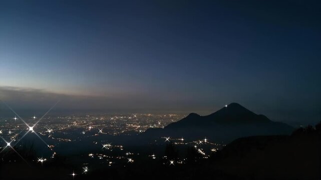Motion graphics of Mount Penanggungan silhouette and Mojokerto cityscape landscape during twilight blue hour. Features animated soft cloud movement and twinkling starburst city lights in East Java.