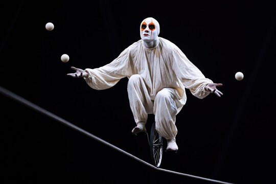 White clown juggler on unicycle riding a tightrope juggling balls for dramatic circus performance poster and banner