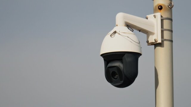 Modern security camera rotating on metal pole against clear sky.