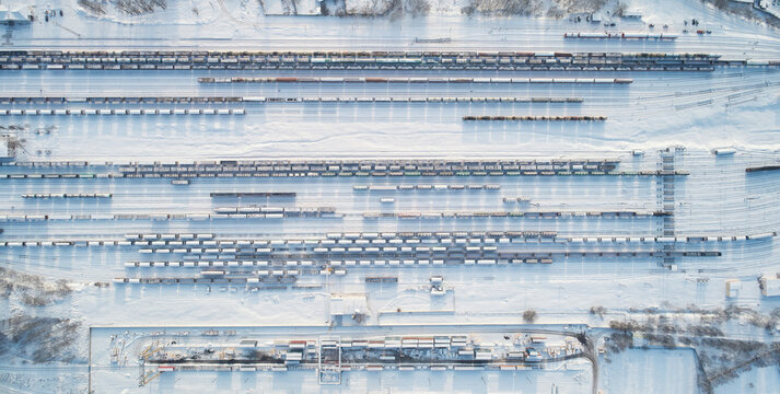 Aerial view of a vast railway yard filled with numerous freight train cars parked on parallel tracks, all blanketed in deep winter snow in Mogilev, Mogilev Region, Belarus.