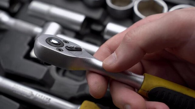 Close-up of mechanic hand holding steel ratchet handle over open professional toolbox with socket set