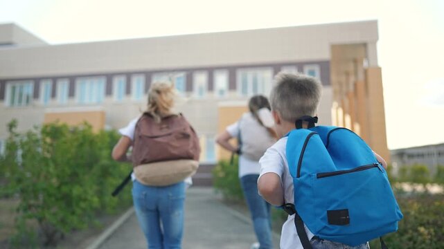 Happy children walking to school with backpacks. kids heading towards school building. children with backpacks smiling. Happy schoolchildren starting day. Children arriving at school with backpacks.
