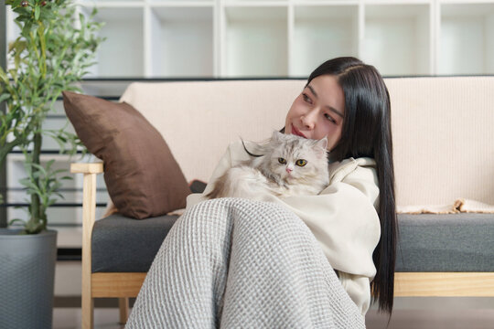 Asian woman cuddling with fluffy cat on floor at home for pet companionship