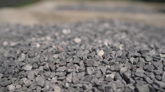 Closeup of gray gravel with scattered beige white stones under natural daylight. Green grass edge at bottom. Landscape design concept.