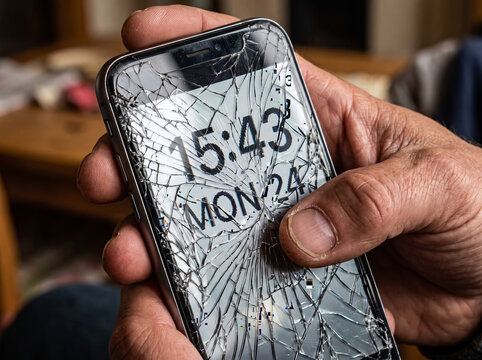 Close up of hand holding damaged smartphone with severely cracked glass screen