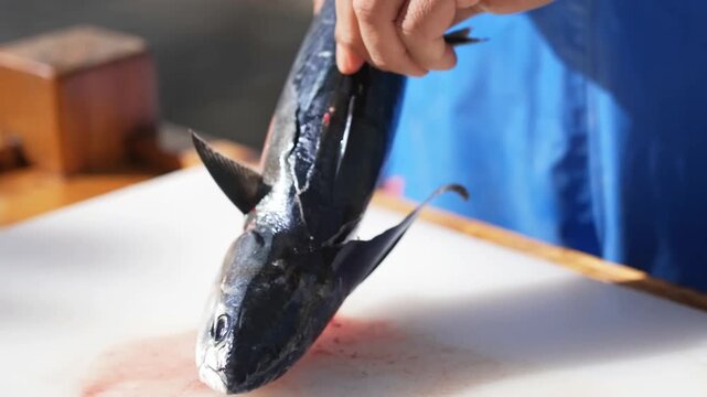 A professional worker uses a sharp knife to clean, slice, and process fresh seafood on a white cutting board aboard a vessel during commercial operations on the open sea