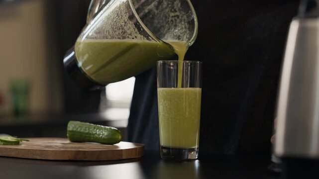 Young adult woman pouring fresh green vegetable smoothie from blender into glass. Video suits wellness brands advertising detox programs or healthy eating campaigns