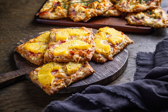 Homemade Flammkuchen with ham, pineapple, and cream cheese on a wooden board