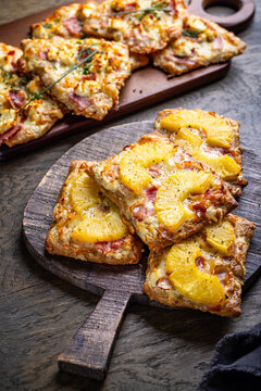 Homemade Flammkuchen with ham, pineapple, and cream cheese on a wooden board
