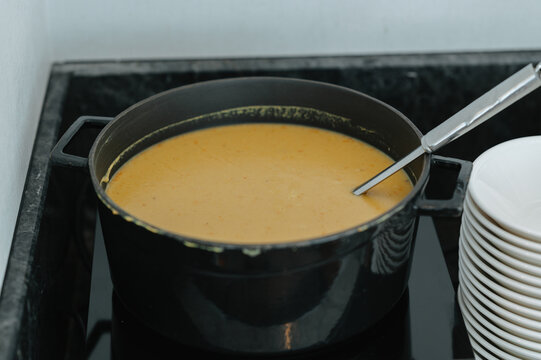 soup being cooked on a warm stove with ceramic pot and metal spoon, top-down view, orange and black hues.