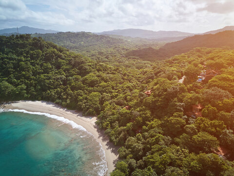 Aerial view of Playa La Redonda with lush tropical forest, sandy beach, and turquoise water under warm sunlight in Tola, Rivas, Nicaragua.