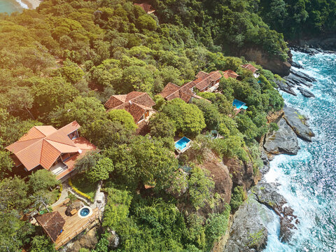 Aerial view of Playa La Redonda resort featuring villas with terracotta roofs nestled in lush tropical forest on a rocky cliff overlooking the Pacific Ocean in Tola, Rivas, Nicaragua.