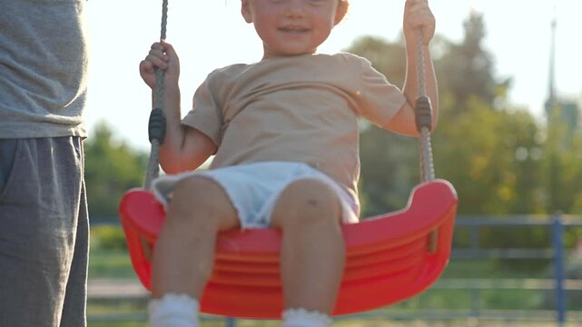 Happy family play together in park. Father pushing child on swing while enjoying outdoor playtime. Family bonding in scenic park setting. Child smiling while play swinging high. Family having fun park