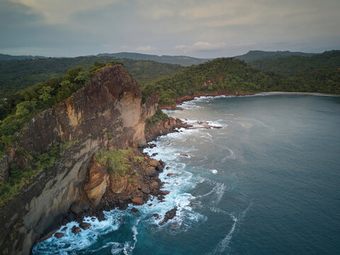 Aerial view of Playa La Redonda featuring rugged cliffs, crashing waves, and lush green hills along the coastline in Tola, Rivas, Nicaragua.