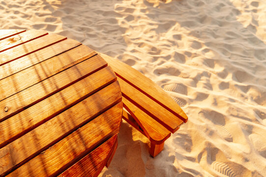 close view of round slatted wooden table and chair on sandy beach in warm golden sunlight near shore