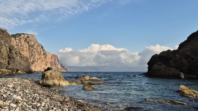 Sea coastline nature, peaceful rocky beach with calm ocean water and towering cliffs under a serene blue sky with fluffy white clouds