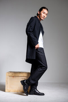 A cool-looking Asian man wearing a black coat was photographed in a studio.