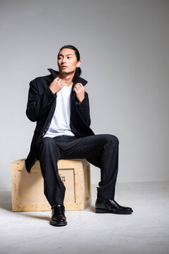 A cool-looking Asian man wearing a black coat was photographed in a studio.