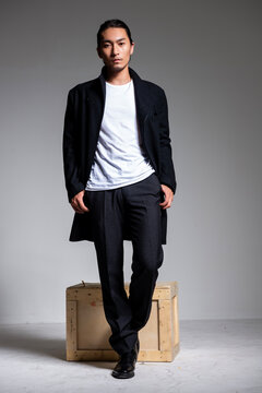 A cool-looking Asian man wearing a black coat was photographed in a studio.