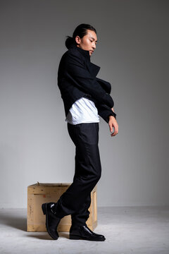 A cool-looking Asian man wearing a black coat was photographed in a studio.