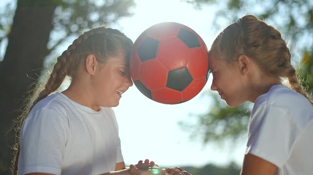children playing with ball in nature. children press soccer ball between heads, laughing together outdoors. childhood moment with ball. children enjoying game nature. Ball play in sunny nature setting