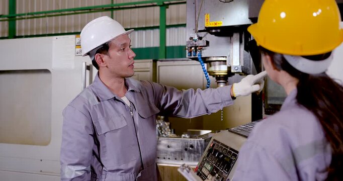 Asian male technician gestures toward spindle area and display, briefing woman engineer on program status, safety check, machining sequence, production workflow in , slow motion.