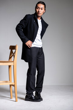 A cool-looking Asian man wearing a black coat was photographed in a studio.