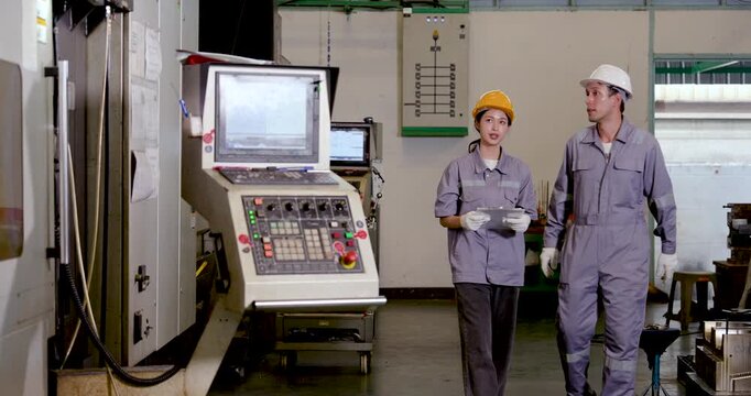 Asian woman engineer briefs male technician near CNC control unit, pointing toward machine area while discussing program status, safety task, production planning, workflow coordination in factory.
