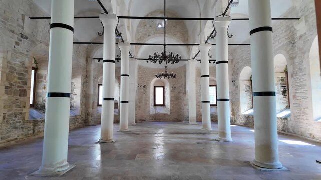 White columns line the spacious, stone-walled interior of the historic Yalı Church in &Uuml;nye, Ordu, featuring arched windows and chandeliers.